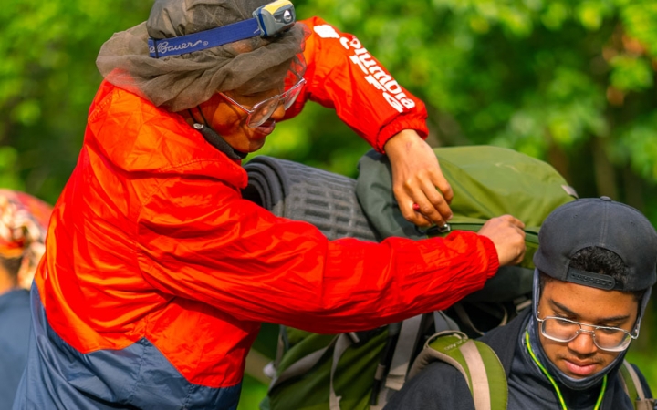 One person adjusts the backpack of another person while outdoors